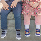 Two children in casual clothing and shoes sitting on a ledge.