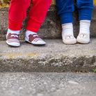 Two children in red and blue pants wearing sock shoes with bear designs on a concrete step.