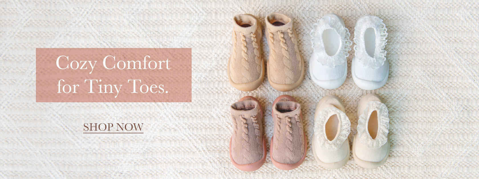 Four pairs of baby Komuello sock-shoes in various shades of pink, tan, beige,a nd white arranged in a row on a textured, light-colored rug.