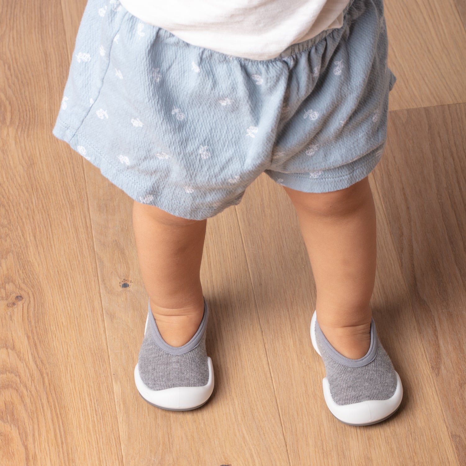 Baby wearing blue shorts and gray soft shoes.
