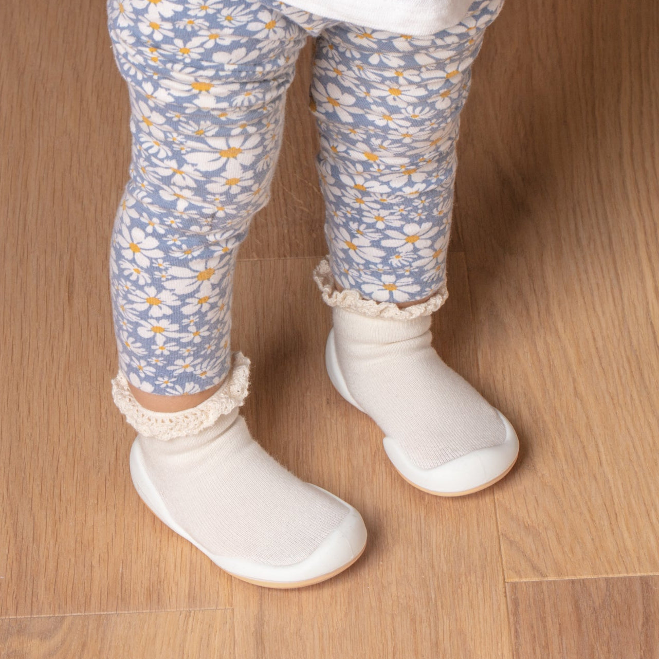 Close-up of a child's legs wearing floral print leggings and white sock-shoes.