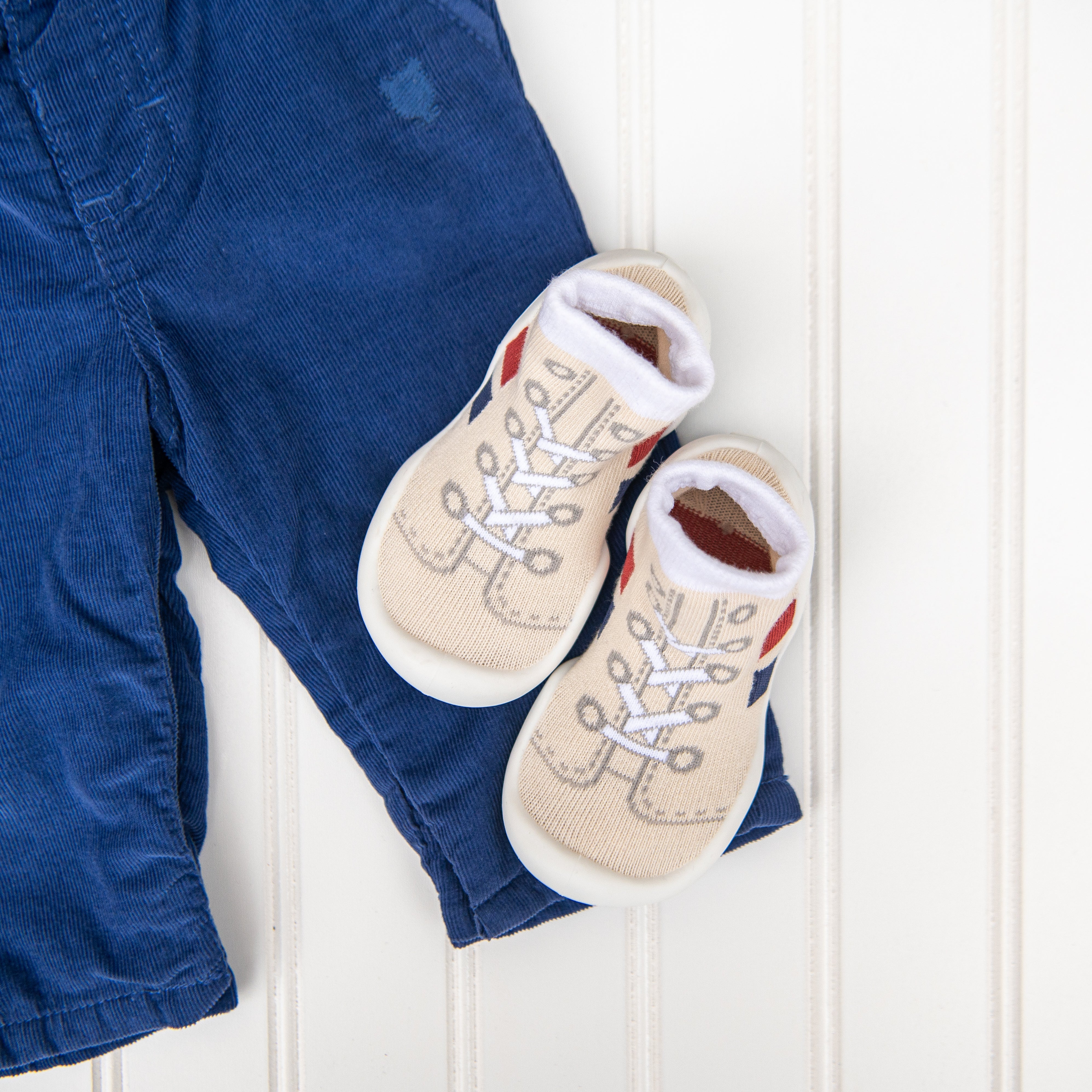 Blue corduroy pants and baby booties on a white wood surface.