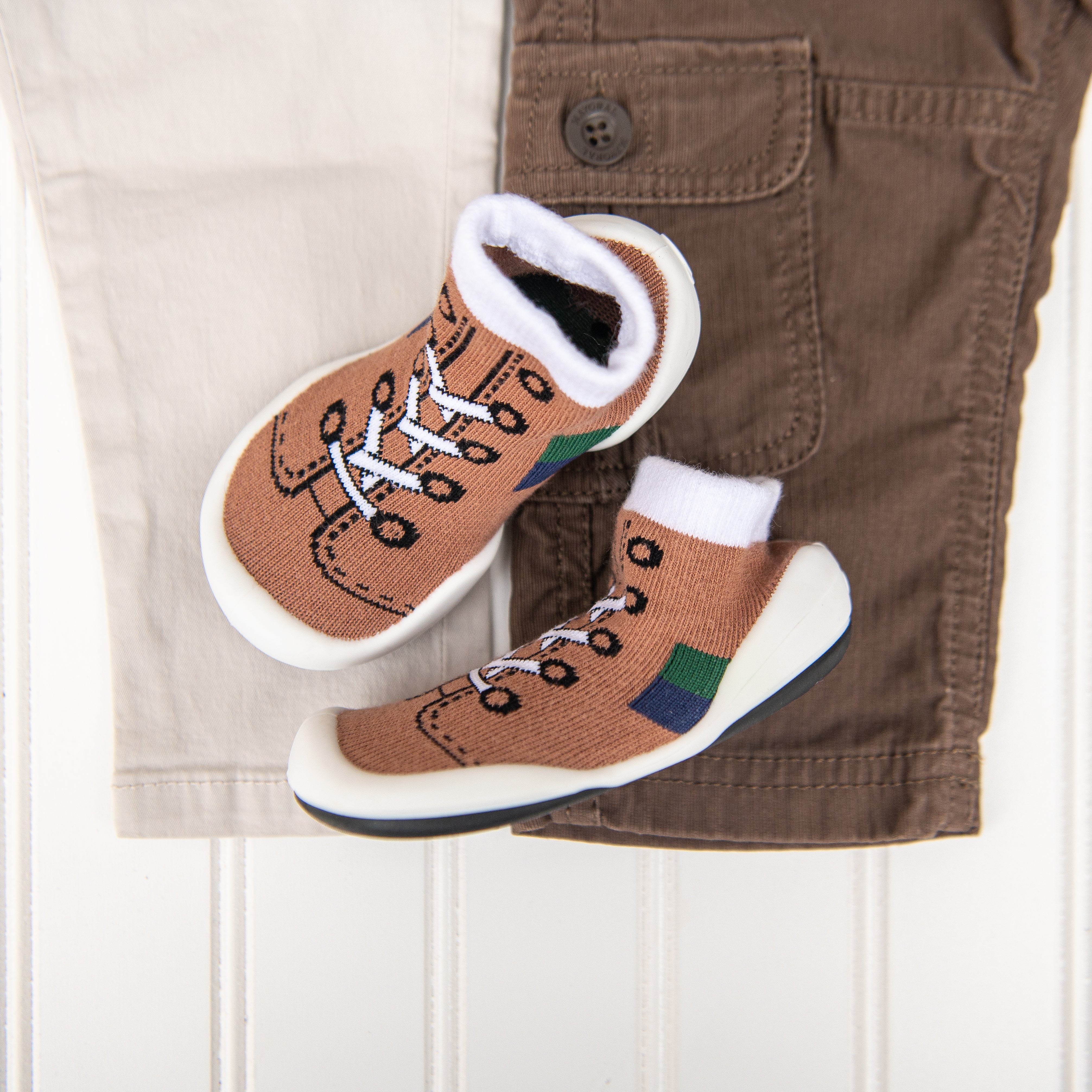 Pair of brown sock shoes atop light-colored and brown pants.