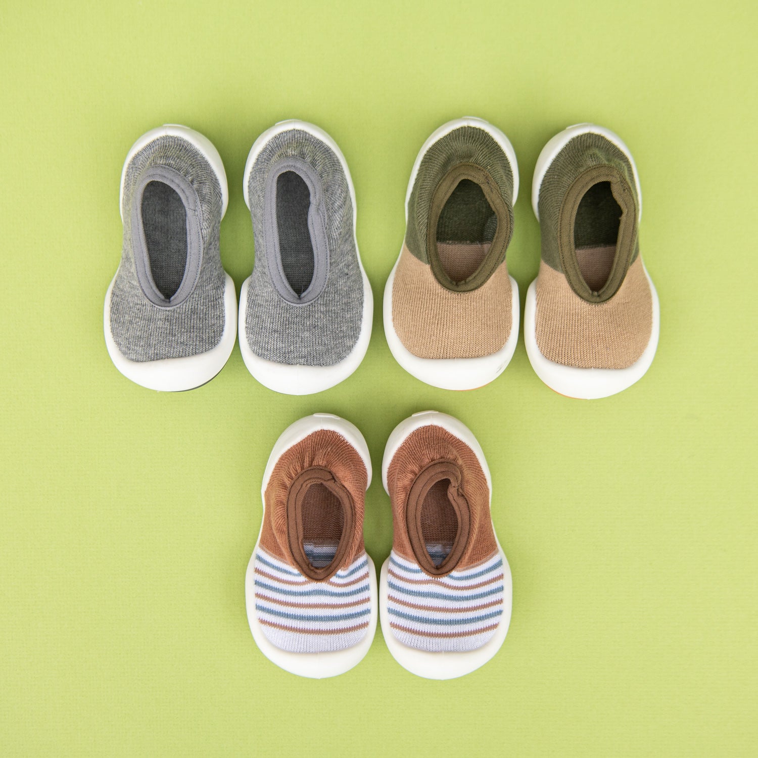Four pairs of baby shoes in a row and one pair of baby shoes below them against a light green background.