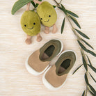 Two plush olive toys, an olive branch, and two baby moccasins on a beige surface.