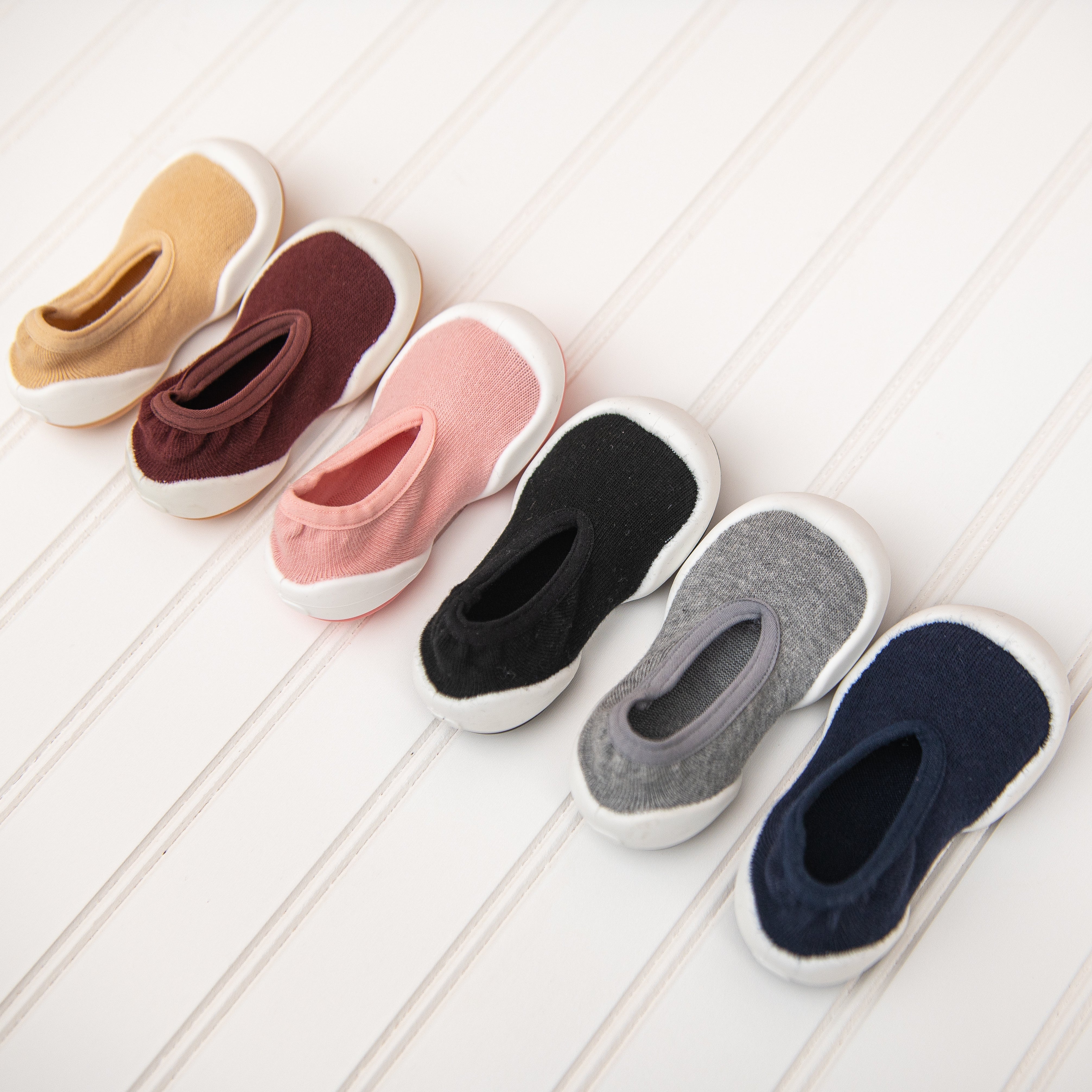 Six colorful baby shoes with white soles, arranged in a row on a white surface.