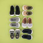 Six pairs of baby walking shoes in various colors, laid out on a light green background.
