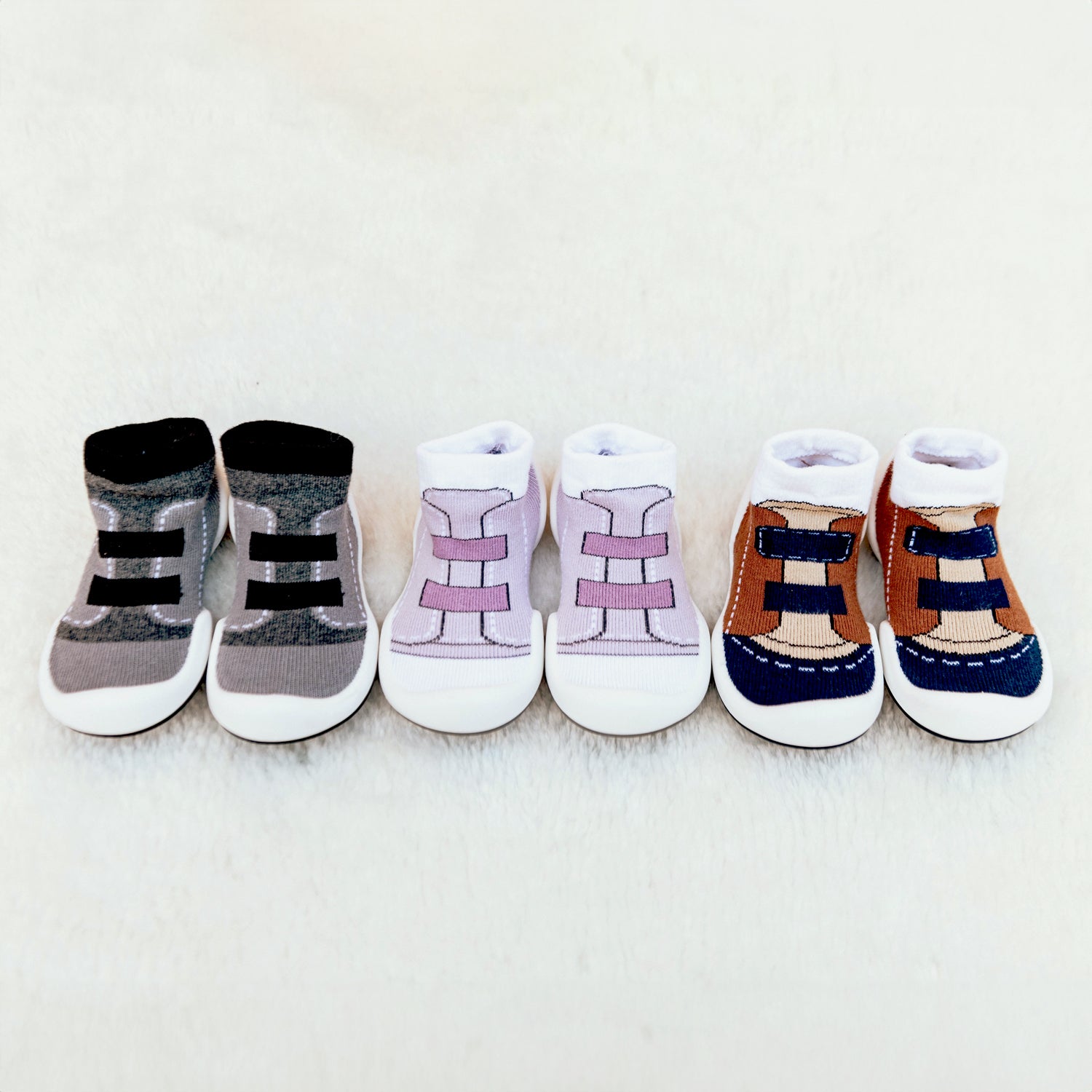 Three pairs of baby socks that look like sneakers in gray, purple, and brown with white soles.