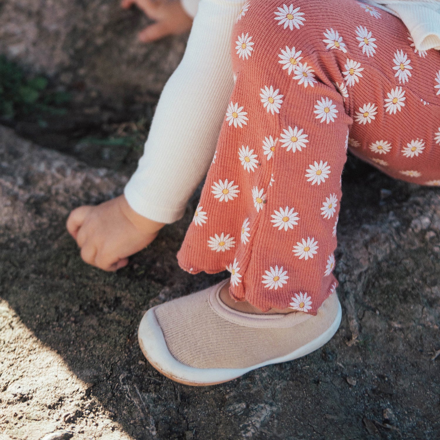 Child wearing pink floral leggings and beige komuello shoes on a rocky surface