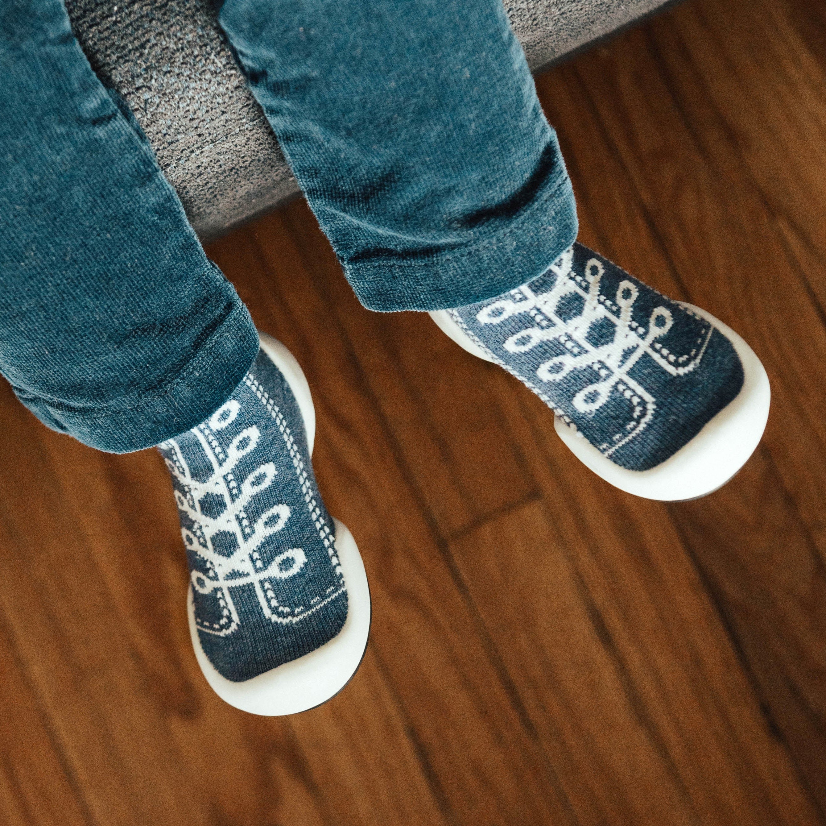 A child's legs and feet wearing blue jeans and blue sock shoes with a white geometric pattern.