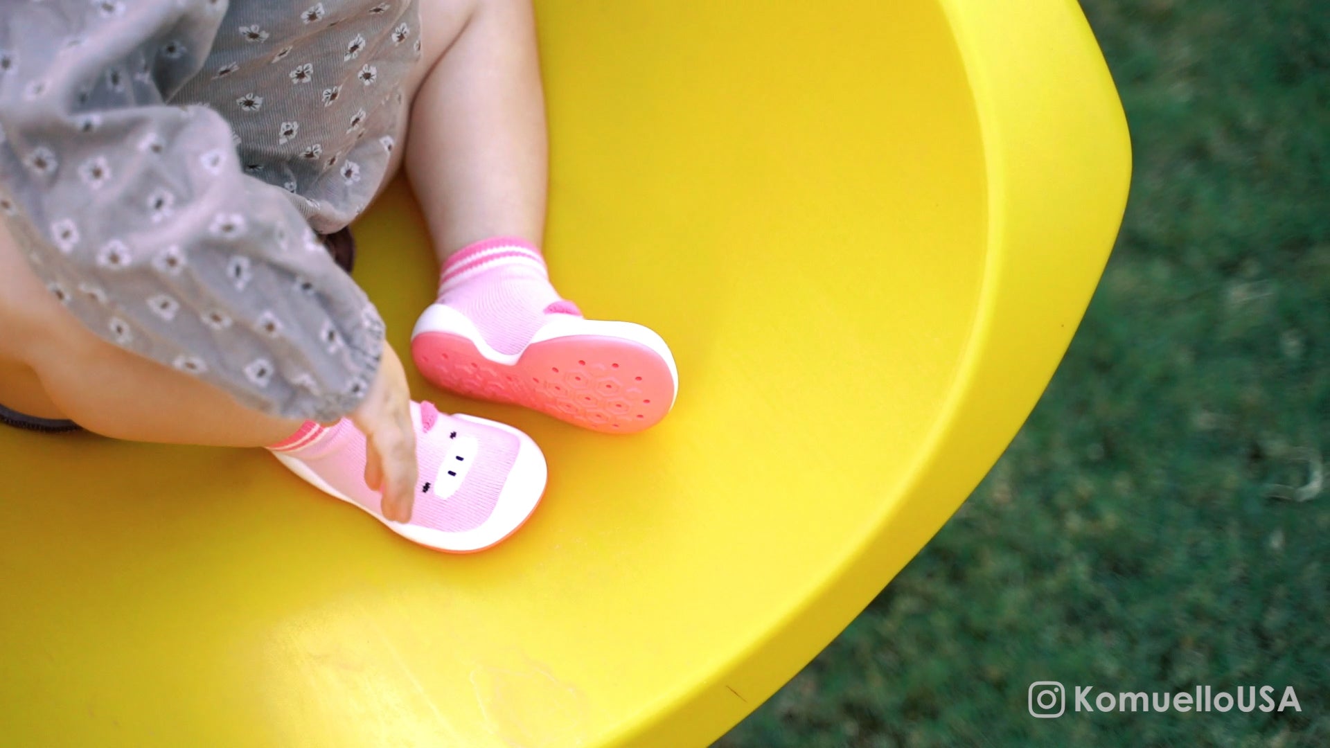Child wearing pink komuello shoes on a yellow surface with grass in the background
