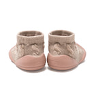 A pair of beige knitted baby shoes with pink soles.