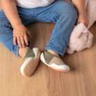 A toddler in jeans and shoes with a pink plush toy, sitting on a wood floor.