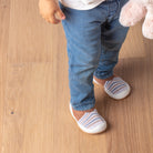 Child in blue jeans and striped shoes, standing on wooden floor.