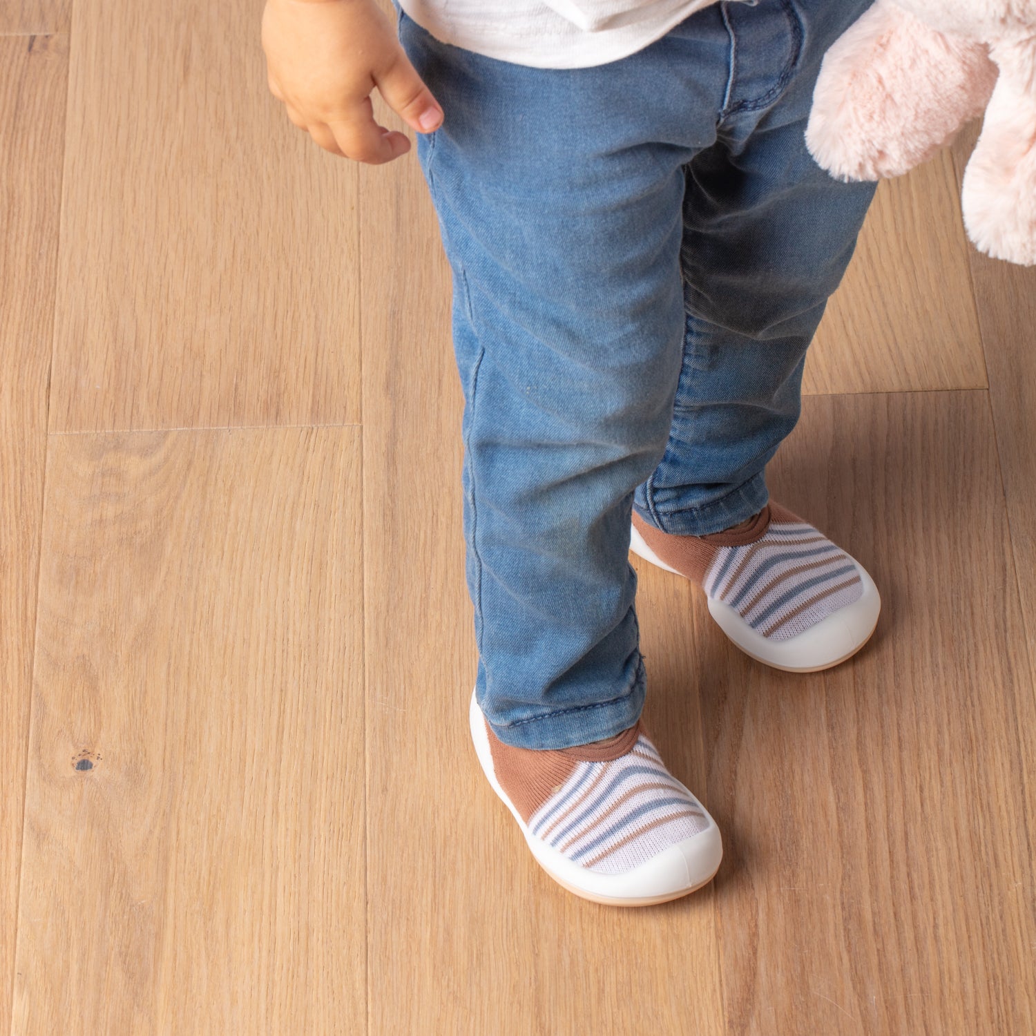 Child in blue jeans and striped shoes, standing on wooden floor.