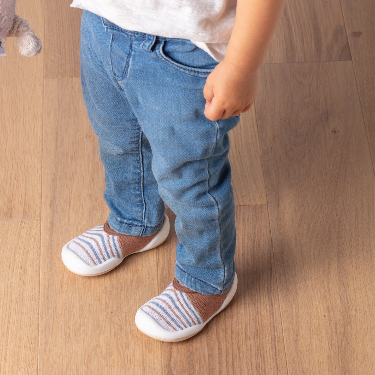 Toddler in jeans and striped shoes standing on wood floor.