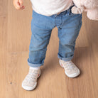 Toddler in jeans and white tee, wearing sneaker socks on wood floor.