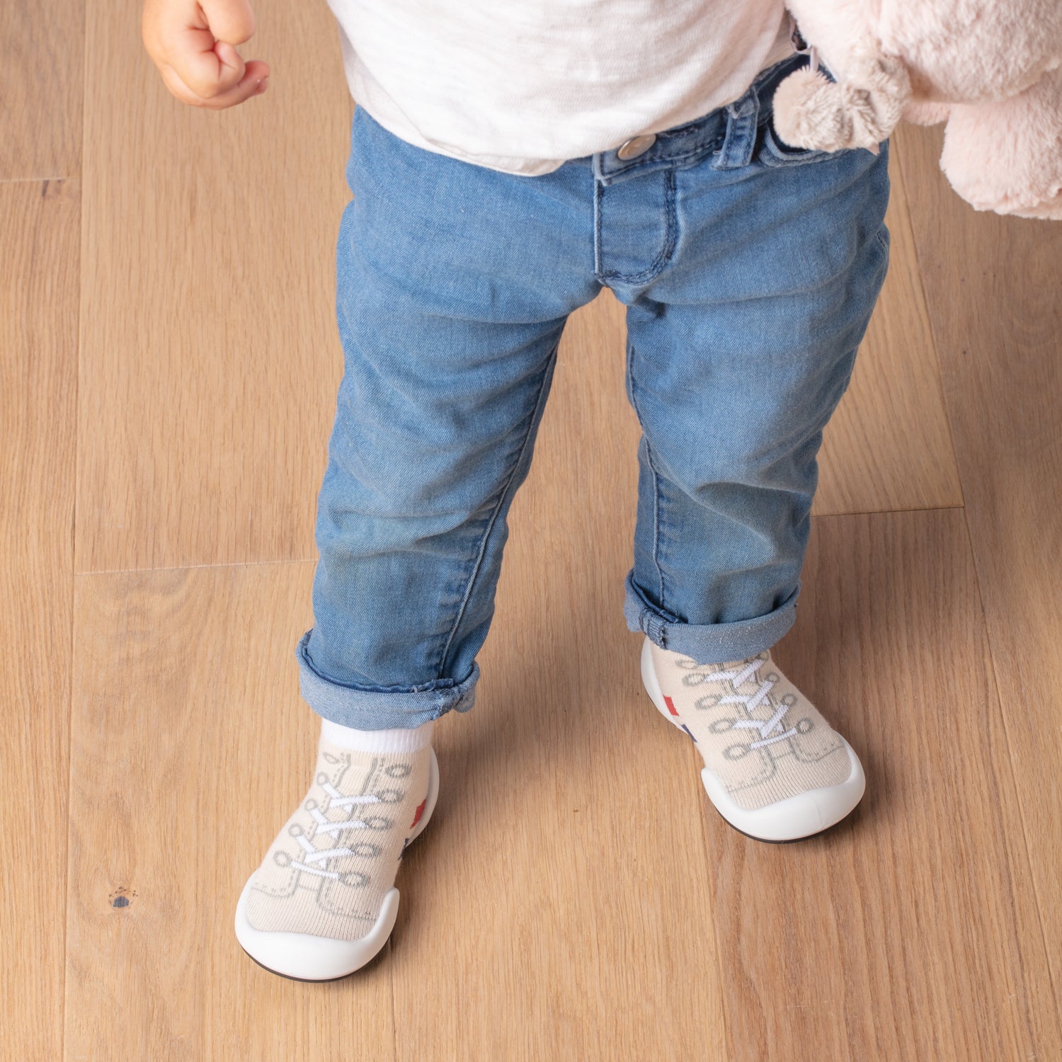 Toddler in jeans and white tee, wearing sneaker socks on wood floor.