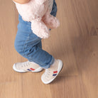 Child in jeans and novelty sneakers, holding a pink stuffed animal.