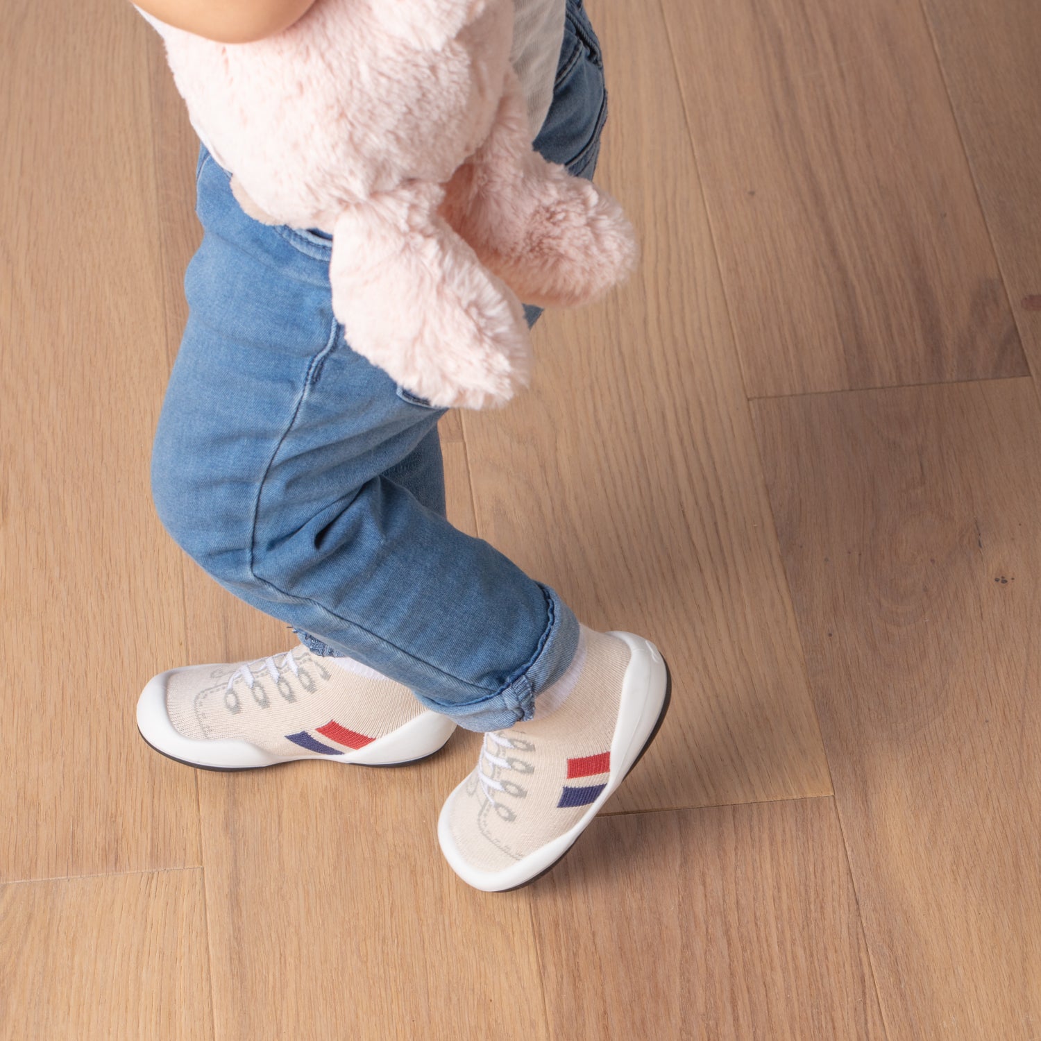 Child in jeans and novelty sneakers, holding a pink stuffed animal.