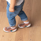 A child in jeans and sock-shoes stands on a wood floor.
