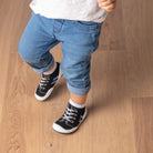 Child standing, wearing jeans and sock-shoes.