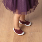 Child's legs and feet, purple dress, maroon shoes, wooden floor.
