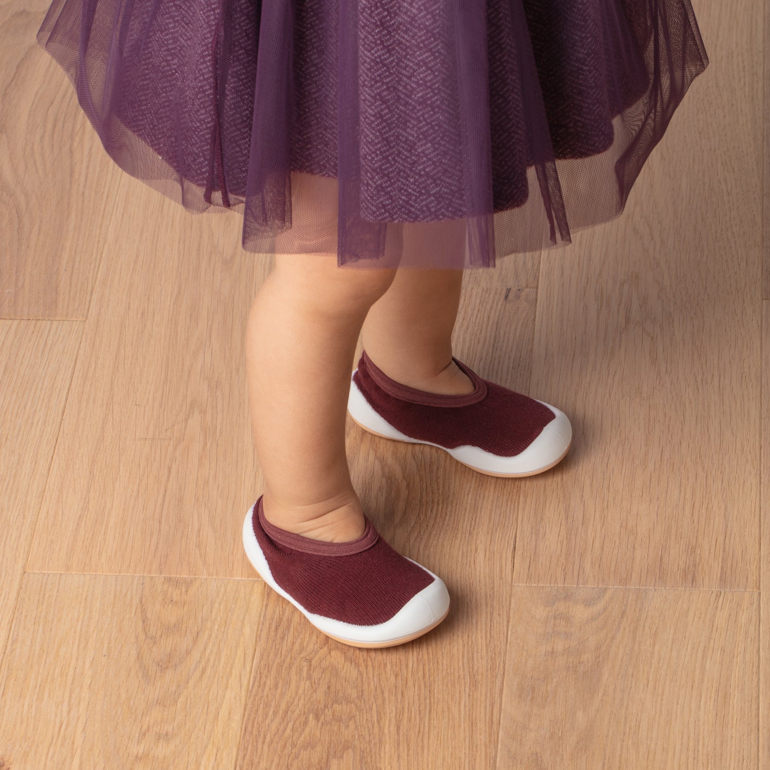 Child's legs and feet, purple dress, maroon shoes, wooden floor.