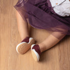 Child in purple tulle skirt, striped shirt, and maroon shoes with white soles on a wooden floor.