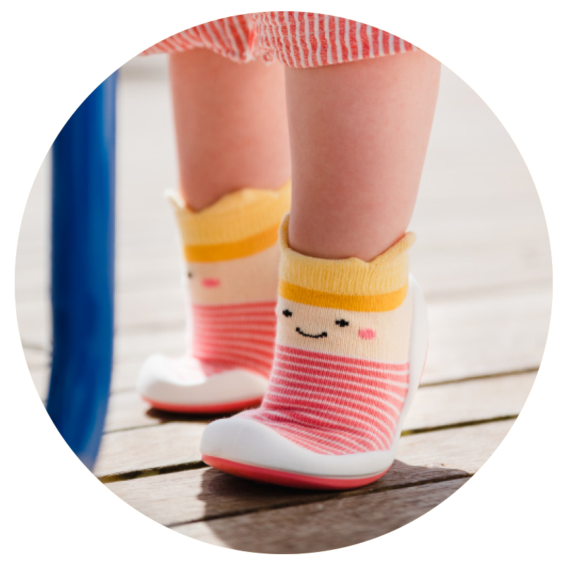 Close-up of kids's legs and pink princess Komuello sock shoes on wooden floor.