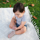 Baby in striped shirt and pink socks sitting on a blanket outdoors.