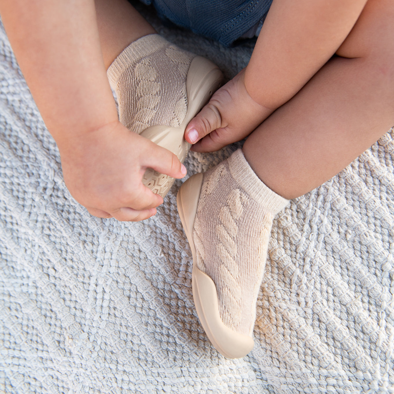 Close-up of baby in tan sock shoes on white blanket.