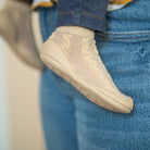 Baby's foot wearing a beige sock-shoe on blue jeans.