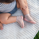 Child in pink sock shoes sitting on patterned blanket.