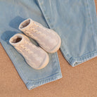 Baby shoes on blue jeans, cork surface.