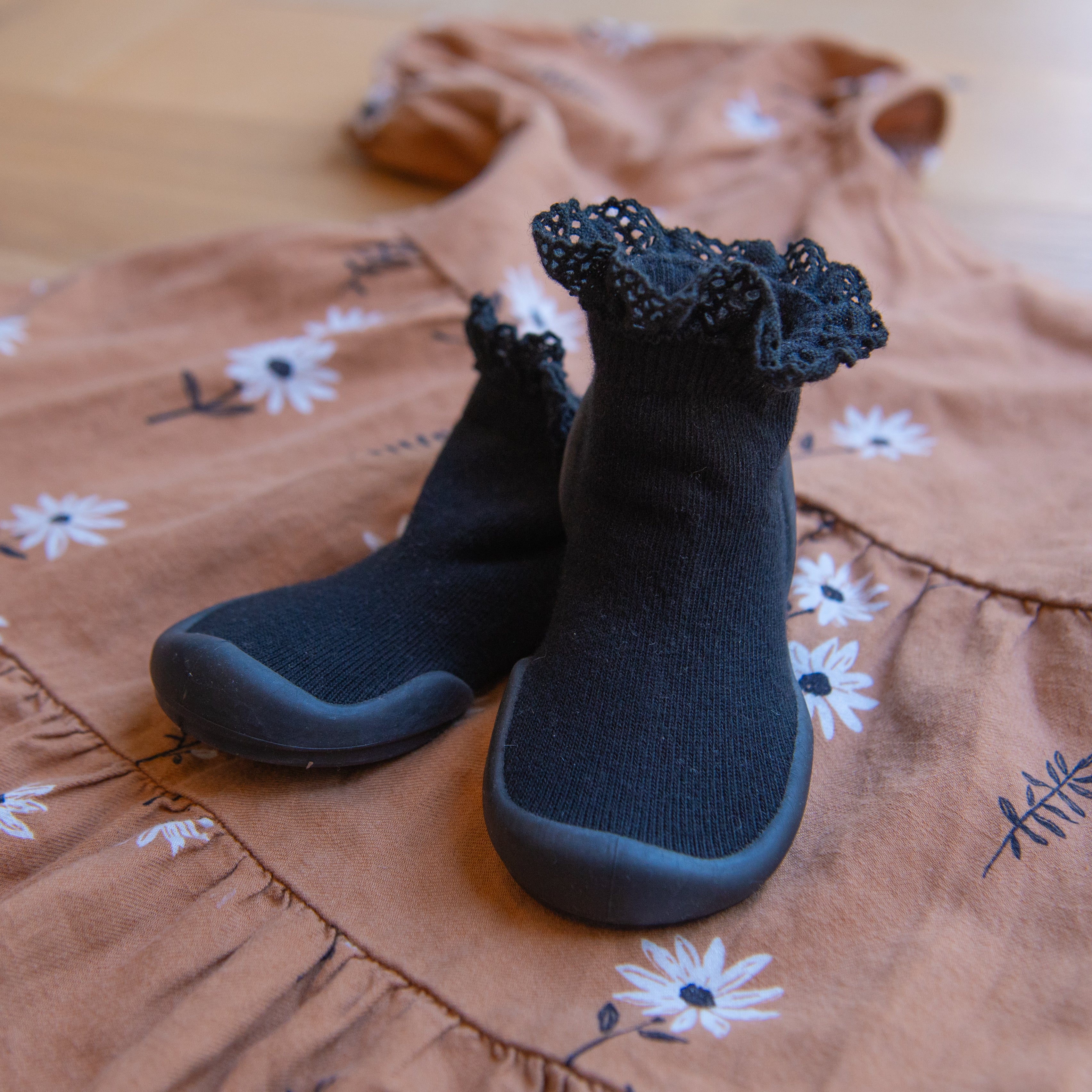 Black baby shoe socks with lace cuffs on top of a brown floral dress.