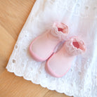 Two pink baby shoes with lace trim on a white eyelet dress.