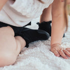 Child on white shag rug, wearing a white sweater, black shorts, and black socks.