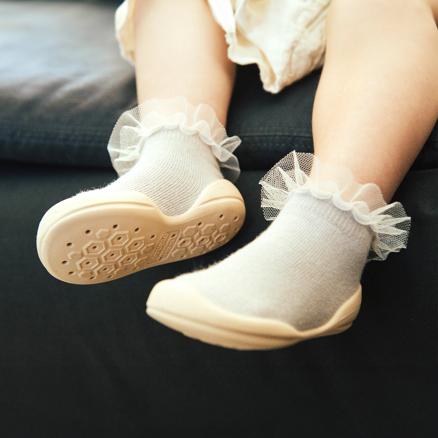 Toddler's feet in white socks with lace trim and attached beige shoes, soles visible.