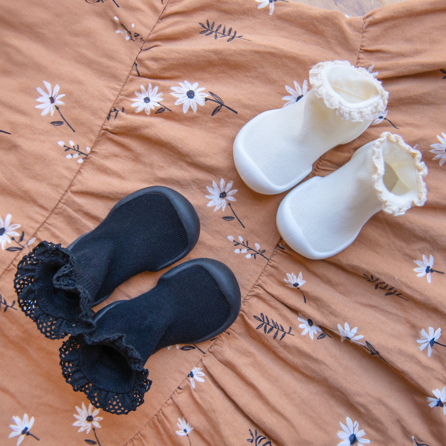 Two pairs of baby shoes: black and white, on a floral-print dress.