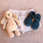 Baby shorts, booties, and plush toy on a brown blanket.