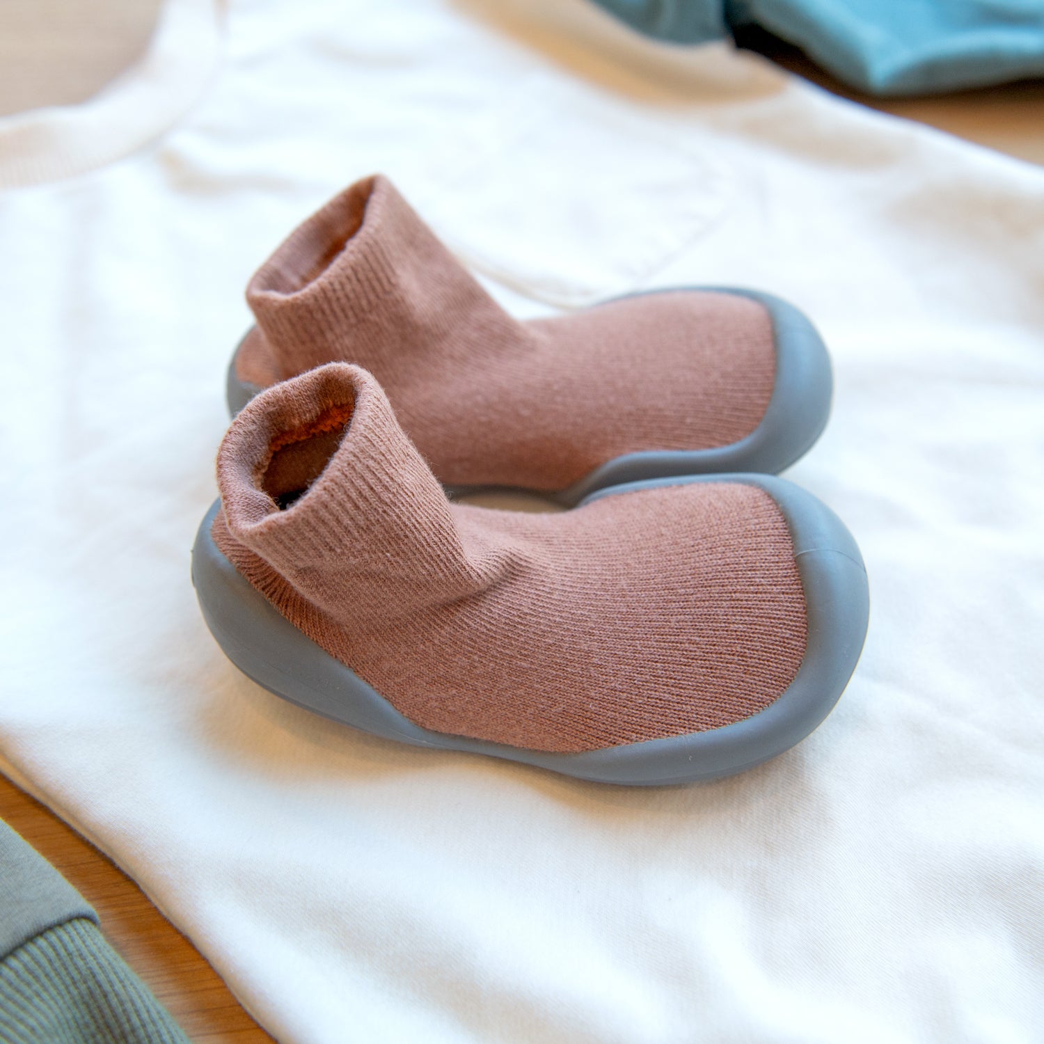 Two brown sock shoes with gray soles on a white shirt.