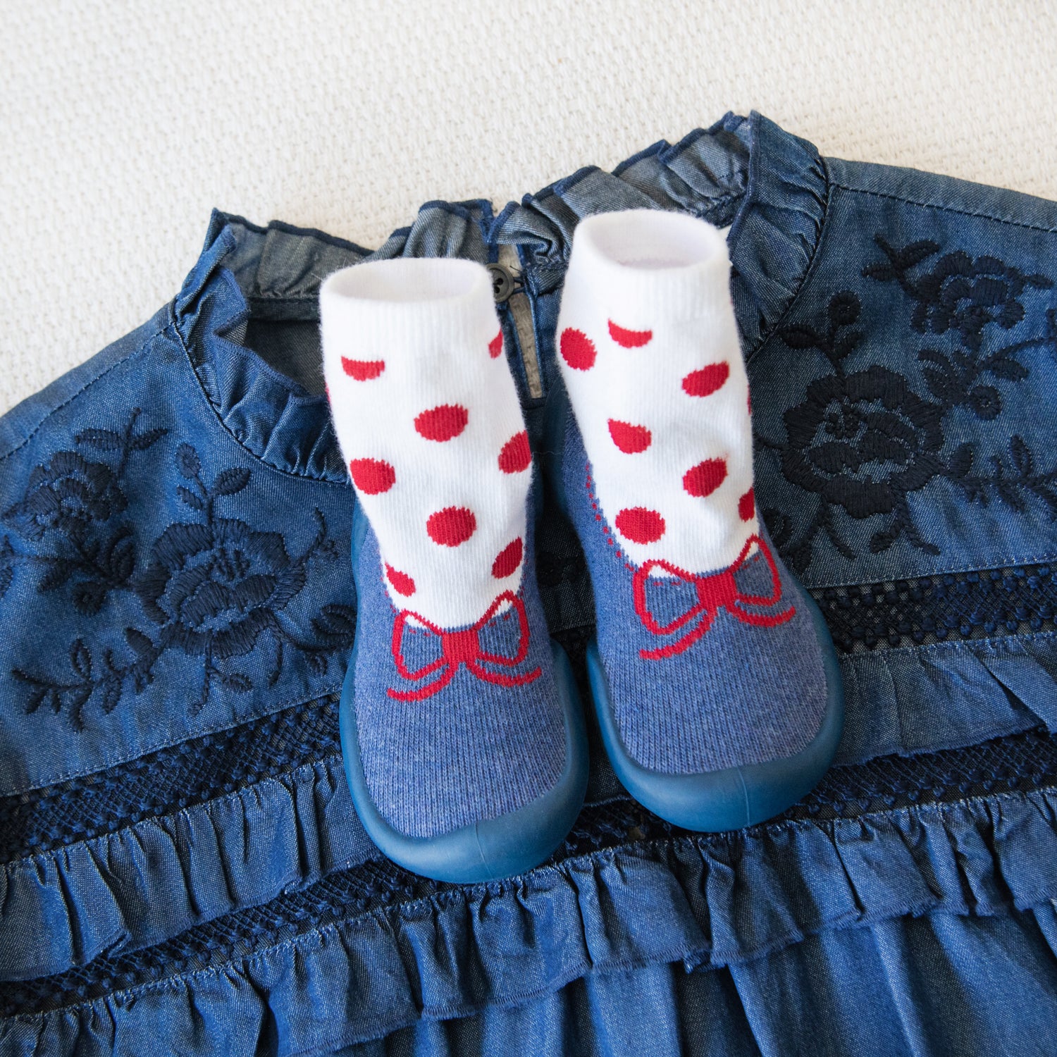 Blue denim dress with ruffled trim, paired with white and red polka dot socks with blue shoe coverings.