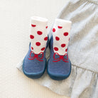 Blue baby shoes with red bows and polka-dot socks on gray fabric.