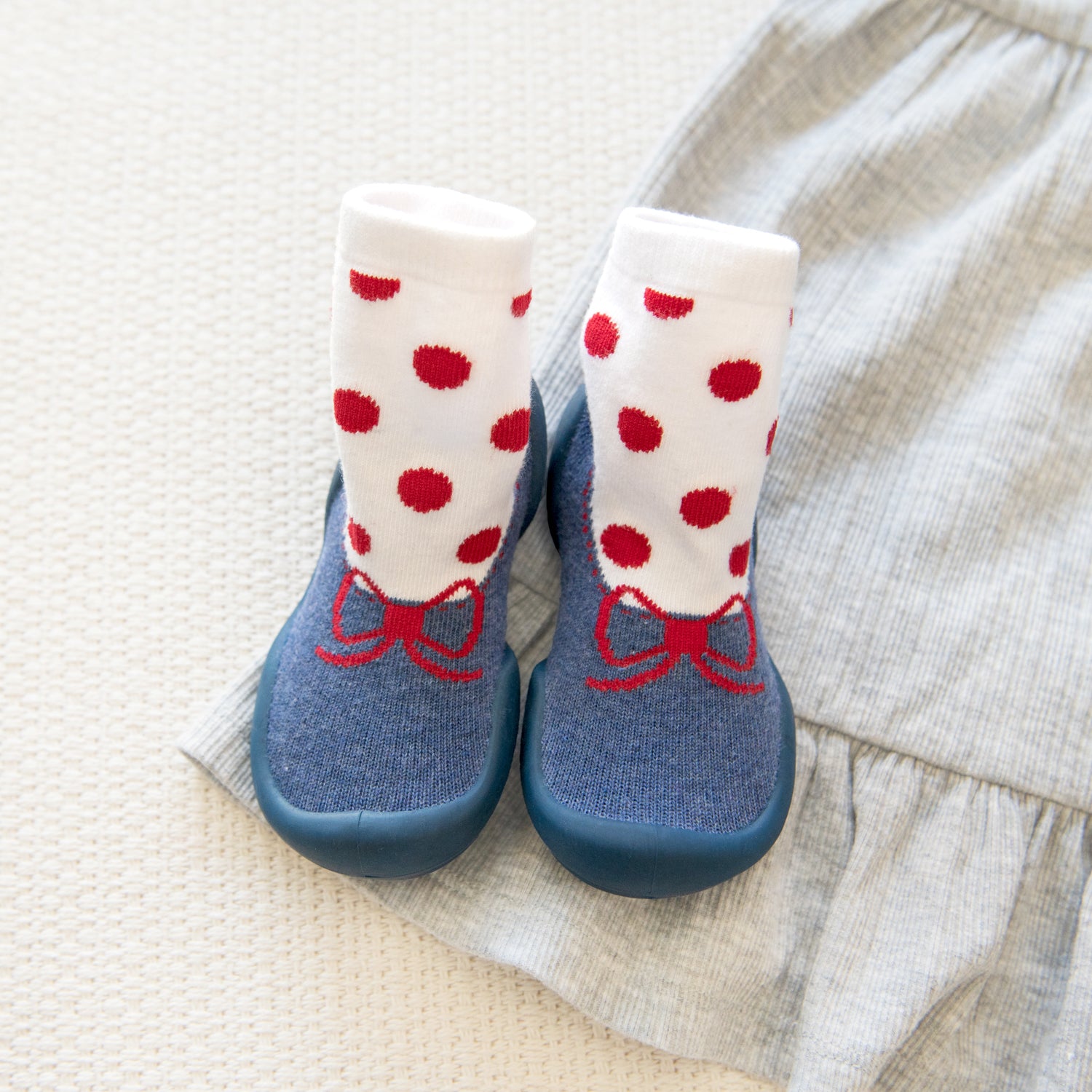 Blue baby shoes with red bows and polka-dot socks on gray fabric.