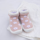 Close-up of pink baby socks with white flowers, rolled white cuffs, and white rubber soles, sitting on a white fabric surface.