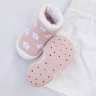 Pale pink baby shoe with white flower pattern and white trim, lying on white quilted cotton.