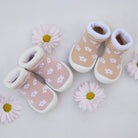 Two pairs of baby slipper socks with white daisies scattered around them and on a white background.
