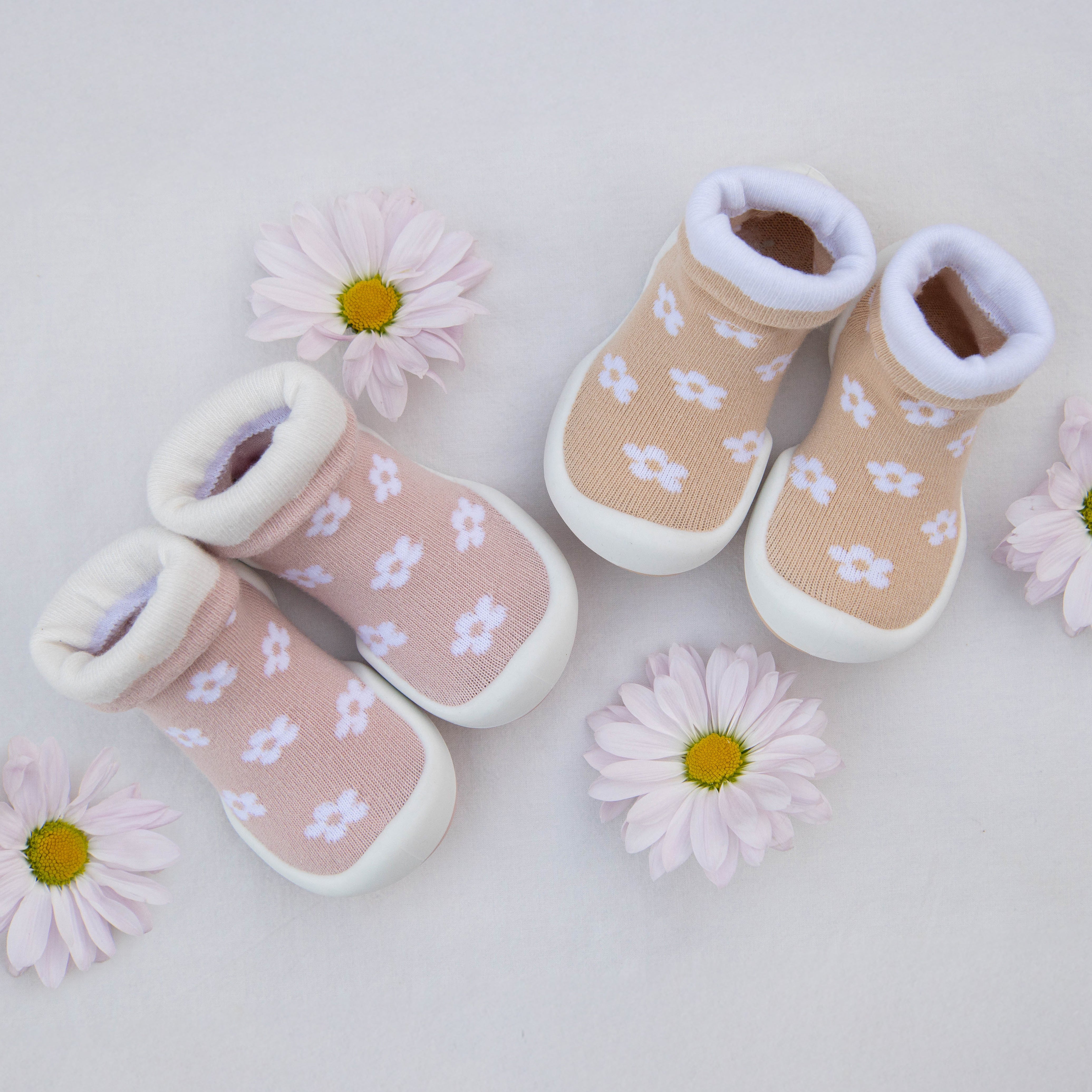 Two pairs of baby slipper socks with white daisies scattered around them and on a white background.