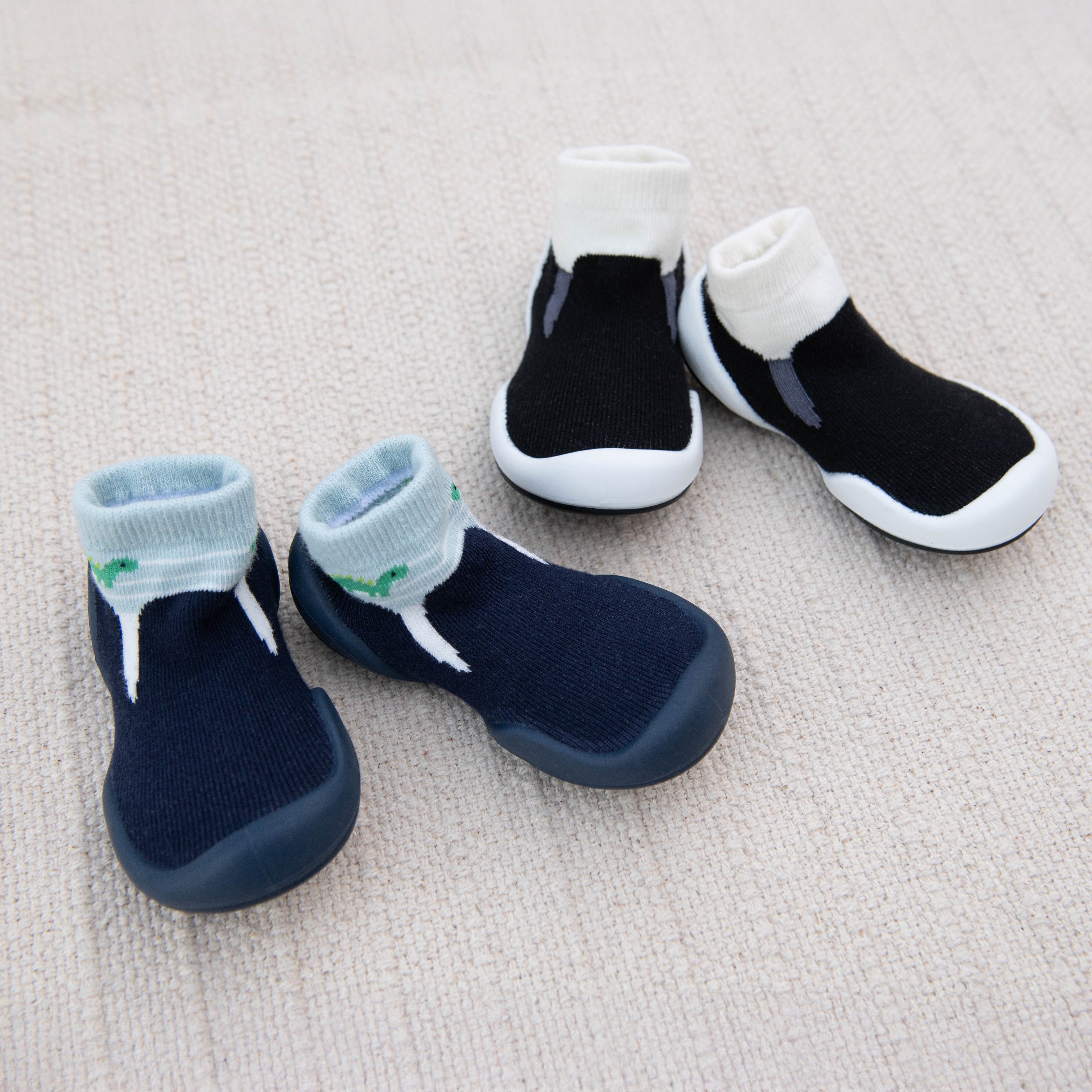 Two pairs of sock shoes, one blue and one black, on a beige fabric.